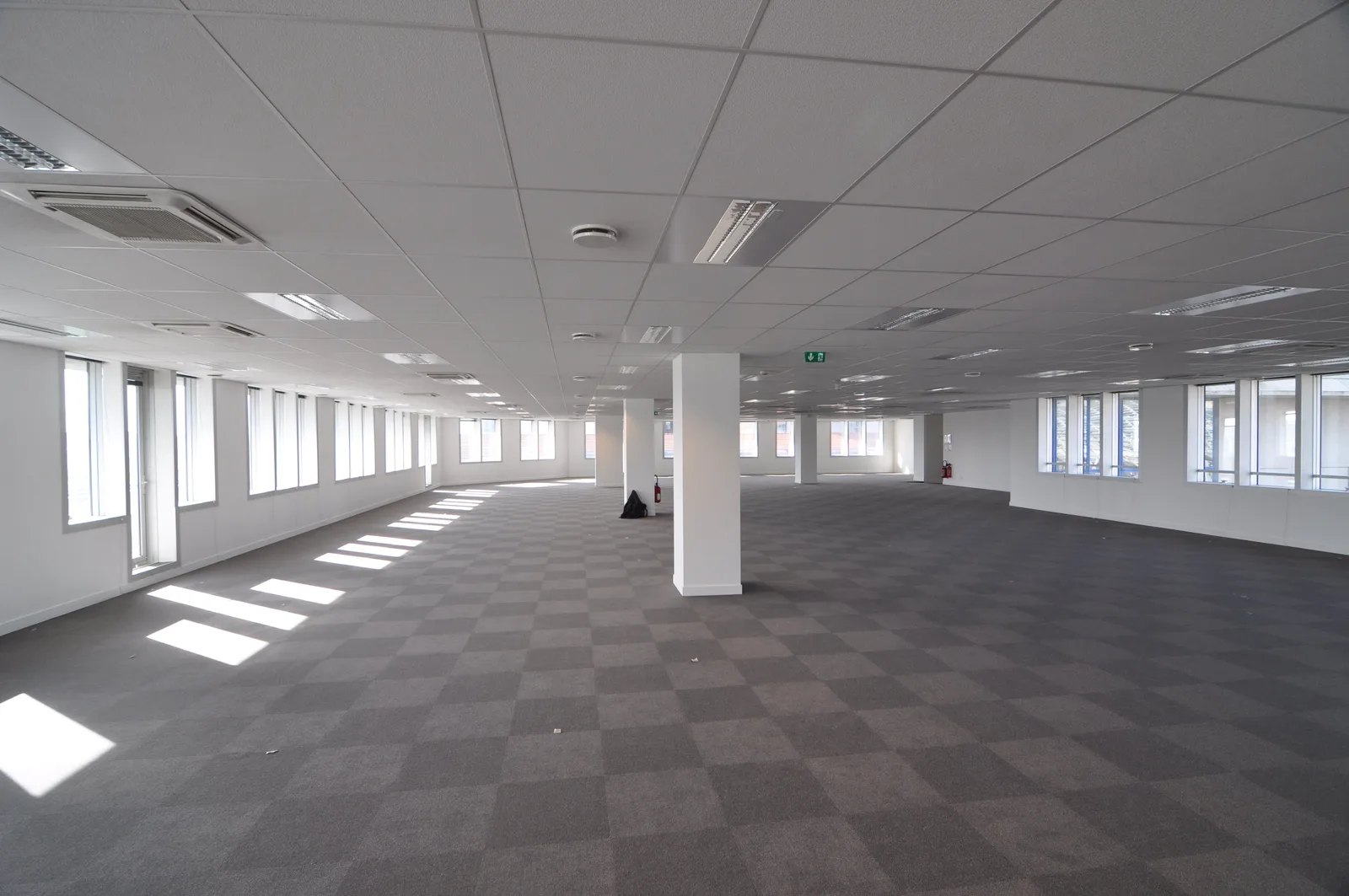Before: large open floor plate showing raw office space with exposed structural columns, extensive windows providing natural light, and vast unmodified empty space