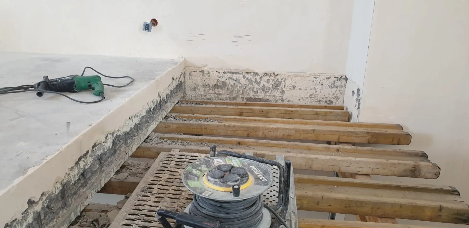 Reinforced concrete floor slab being cut to create duplex staircase opening, exposed ribbed construction with aggregate fill, cutting tools on concrete surface