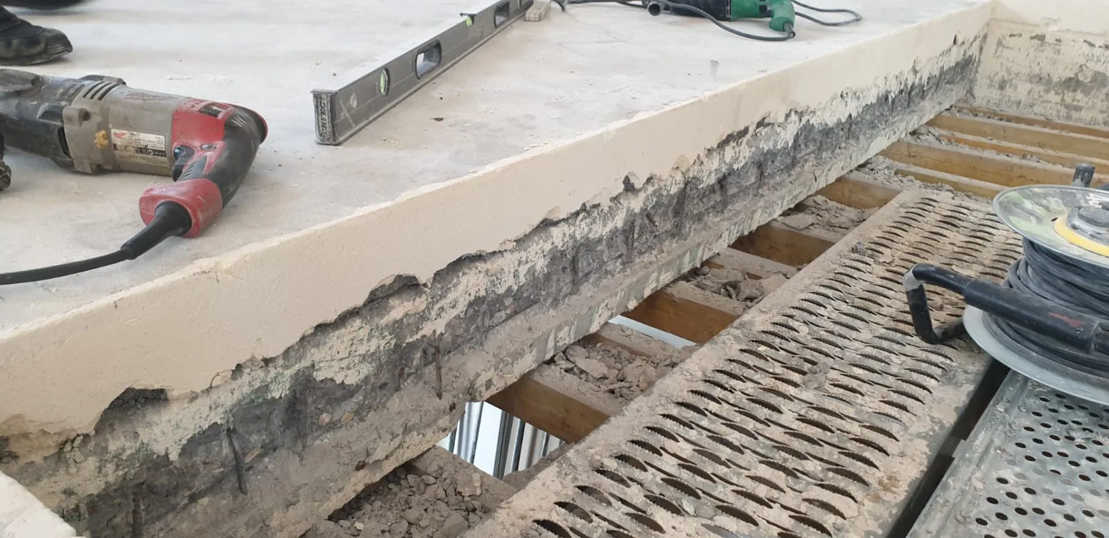 Close-up of concrete slab edge after cutting showing clean structural cut line, exposed aggregate cross-section, spirit level and rotary hammer on surface