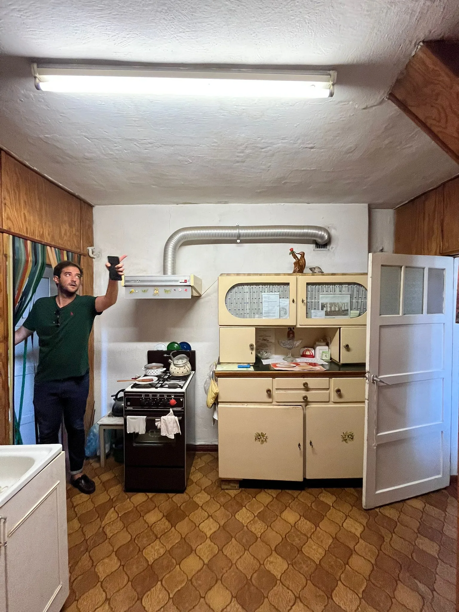 Before: existing condition upper-level living room photo with aged timber truss structure, traditional mortise-and-tenon joinery visible, grey sofa, wall-mounted TV, and roof windows for daylight