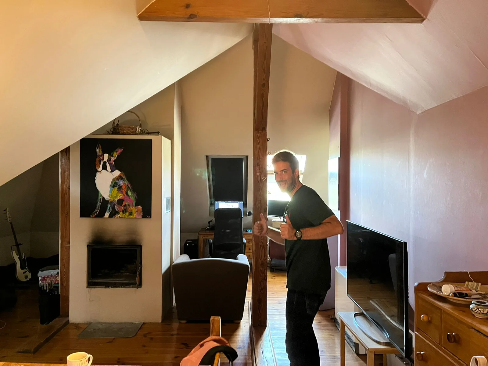 Before: pre-renovation lower-level kitchen photo with 1960s cream enamel kredens cabinet, freestanding gas cooker, patterned vinyl flooring, and wood-panelled plywood walls under attic slope
