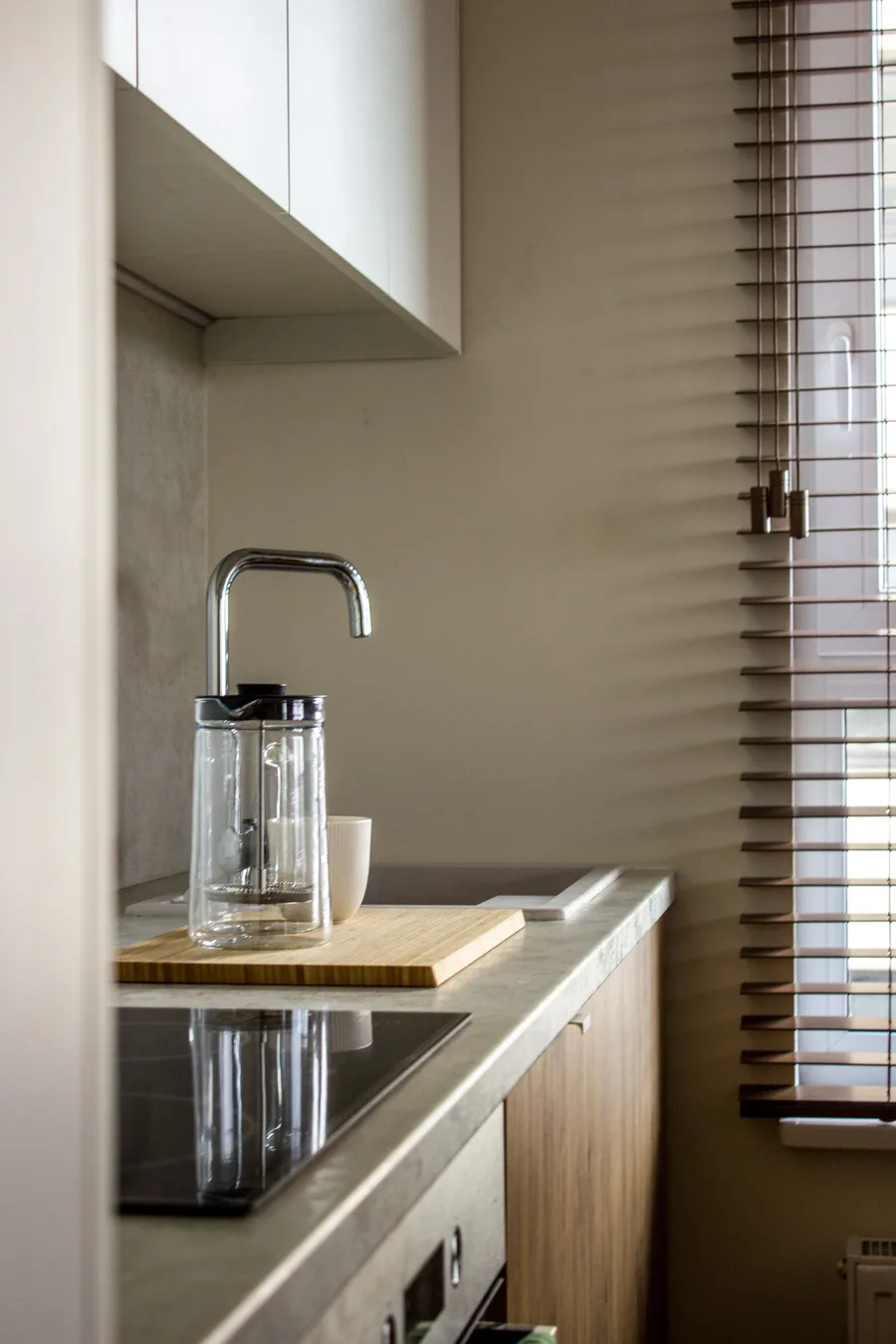 French press on concrete countertop close-up with venetian blind shadow stripes creating dramatic light pattern across surface
