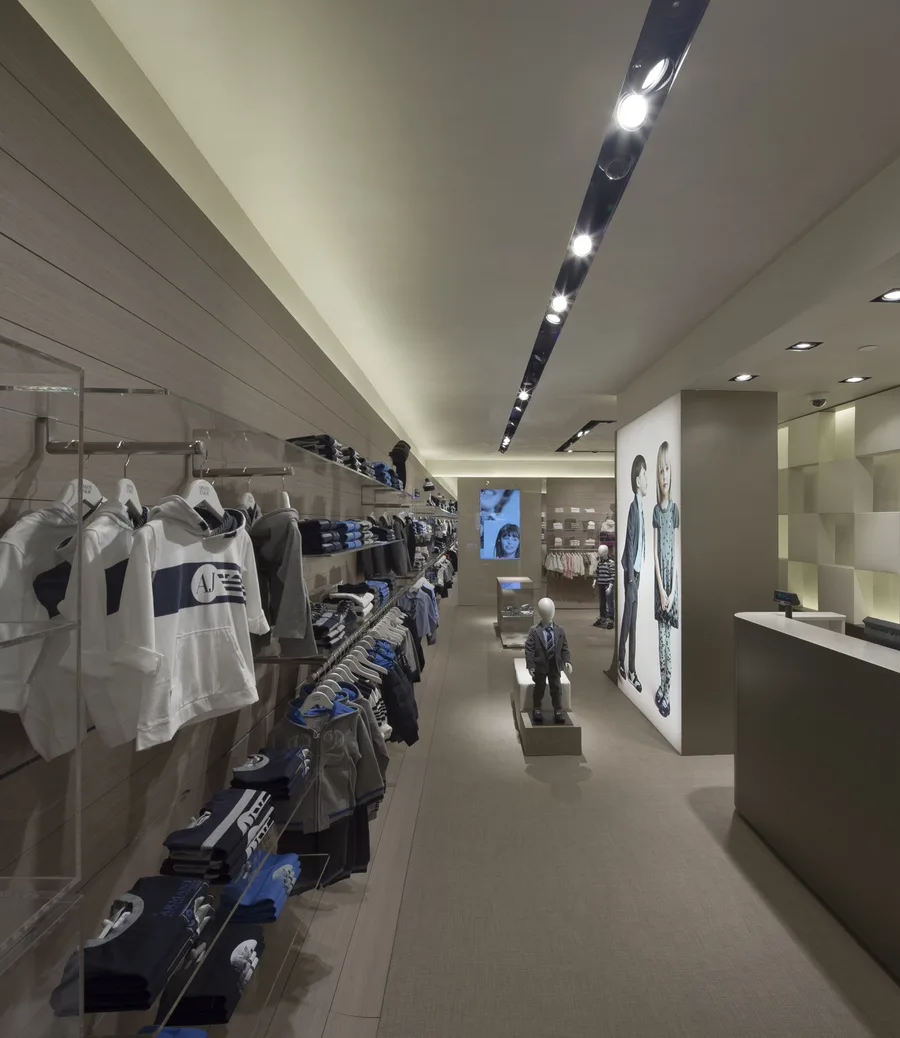 Interior: Barcelona boys corridor with dramatic angular recessed black beam lighting creating geometric gallery-like patterns above merchandise displays