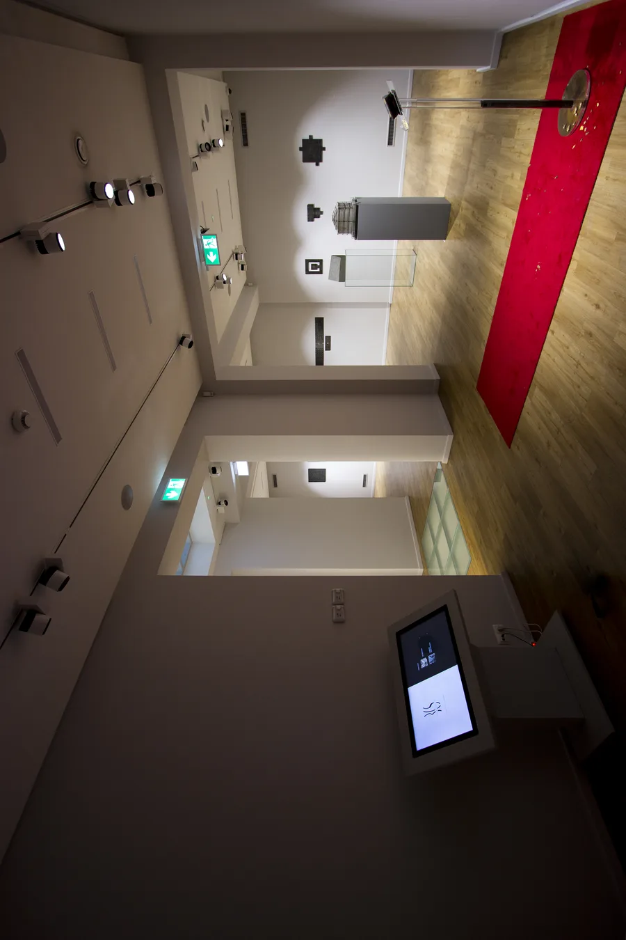 Interior: exhibition gallery space with custom modular display podiums and glass enclosures presenting sculptures on clean white museum-grade epoxy resin concrete-finish surfaces