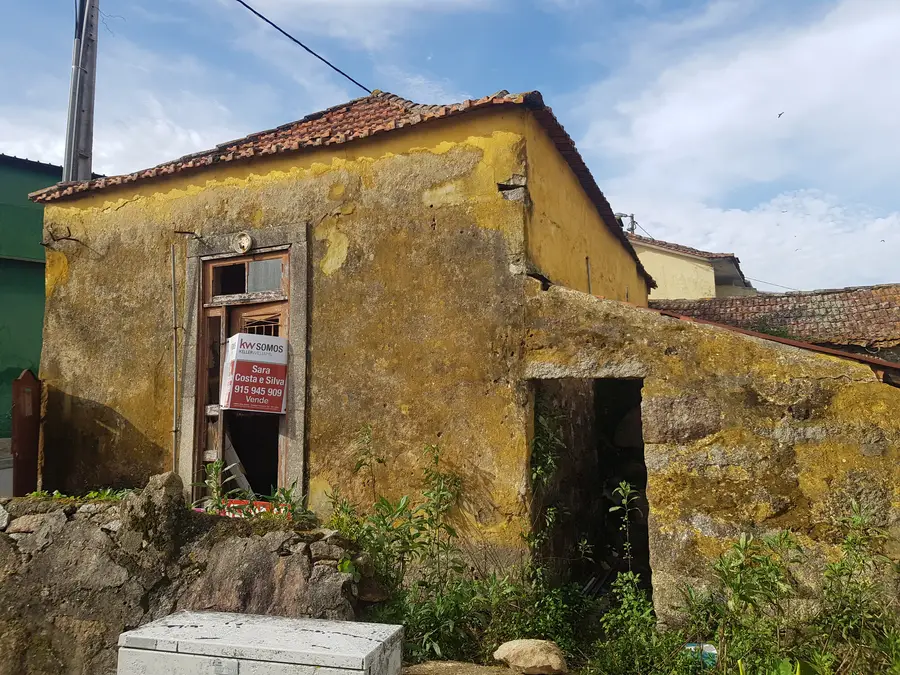 Before: street corner photo with real estate For Sale sign showing the granite building in its Canidelo village context on Rua do Barroco before purchase and rehabilitation