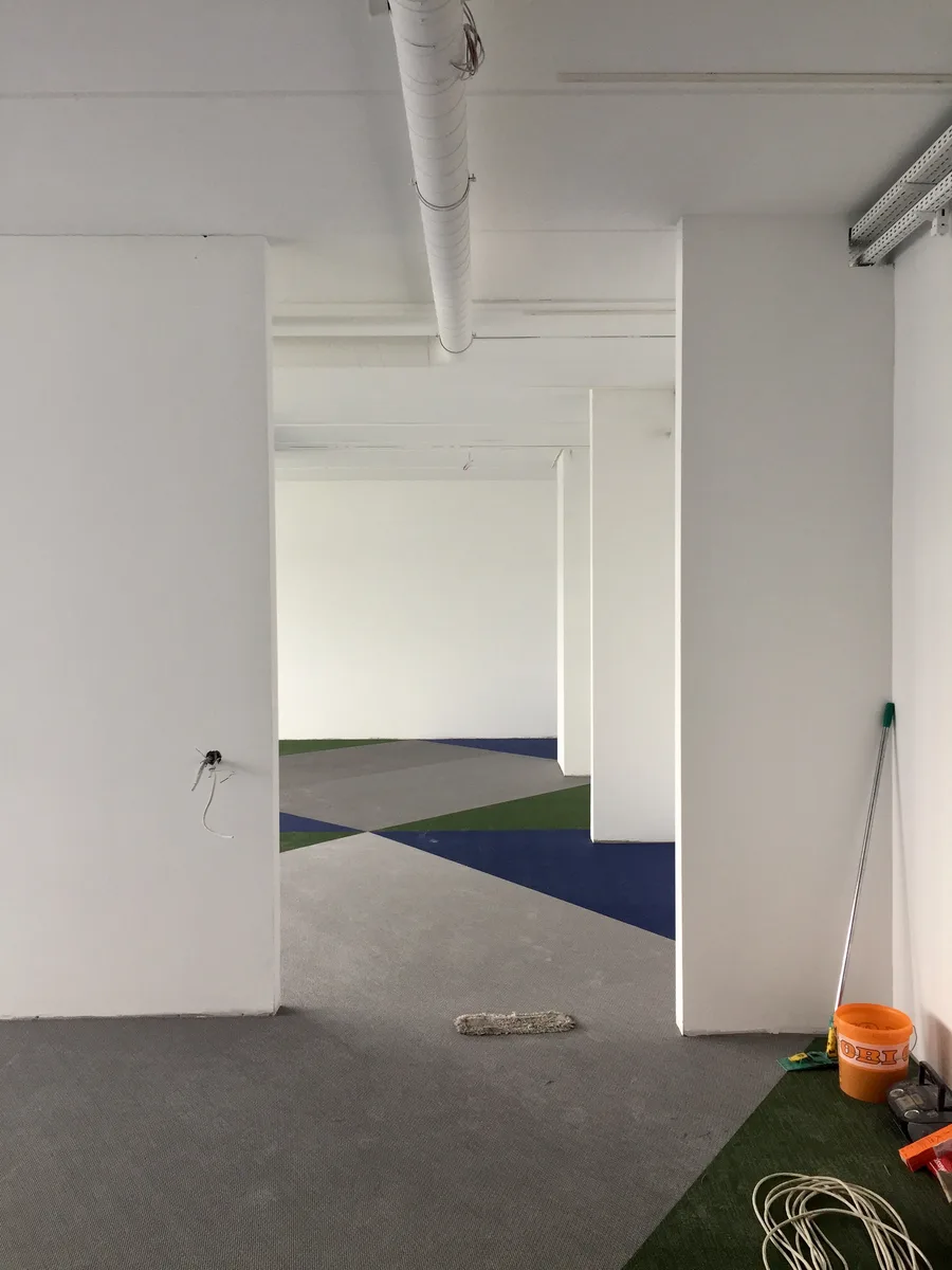 Mid-construction photograph showing exposed floor ducting and infrastructure systems before the woven vinyl floor overlay, revealing the building services coordination