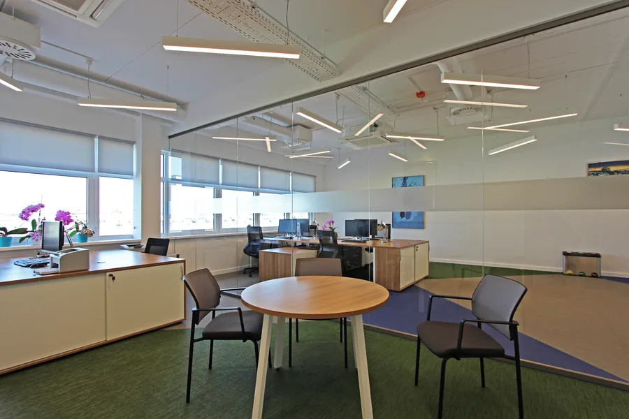 Informal meeting corner with round natural wood table adjacent to a glass-partitioned office, showing the flexible collaboration zones throughout the floor plate