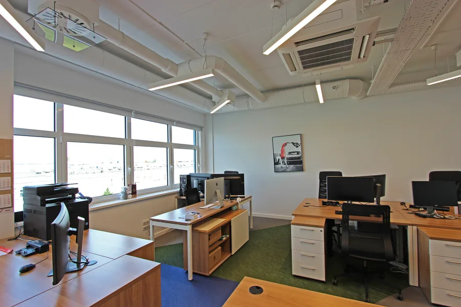 Reception and common area with open-plan layout, multiple desk clusters, pop-art print on wall, glass partition to corridor, and woven vinyl floor