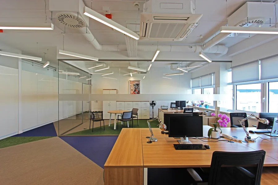 Workstation detail showing ergonomic seating, white desks with natural wood tops, and the three-colour woven vinyl floor pattern