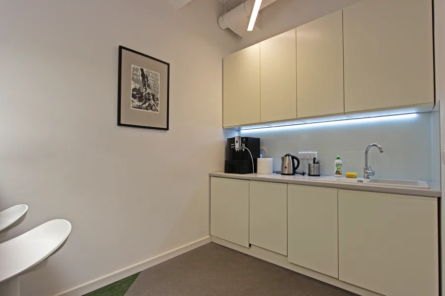 Kitchenette area with LED backsplash, cream cabinetry, and the warm material palette that distinguishes the social spaces from the working zones
