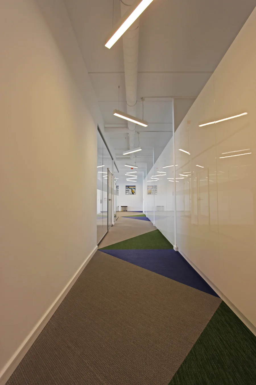 Portrait corridor perspective with glass-walled offices on both sides, frosted privacy bands, and the three-colour woven vinyl floor pattern