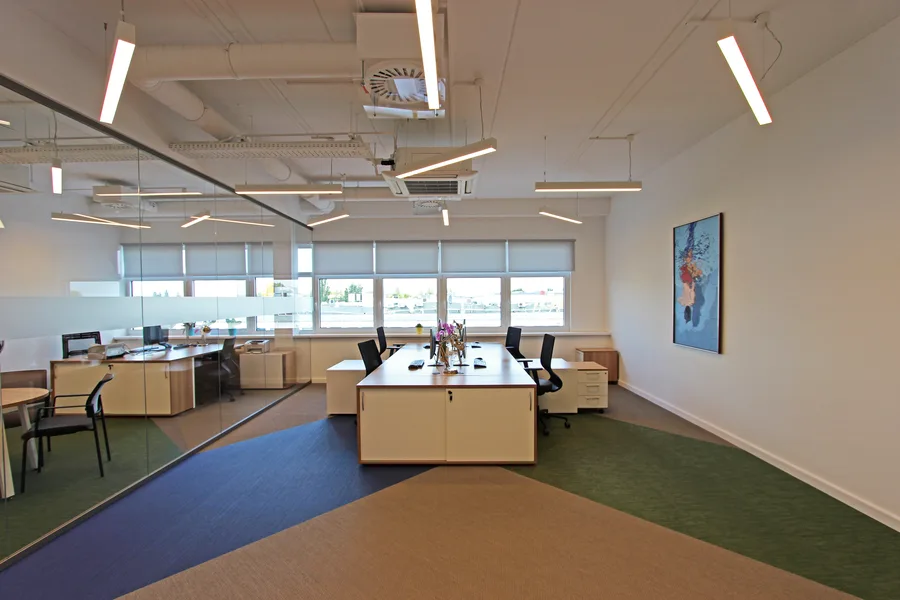 Open office workspace with glass meeting corner, workstation island, woven vinyl floor in three colors, and natural window light