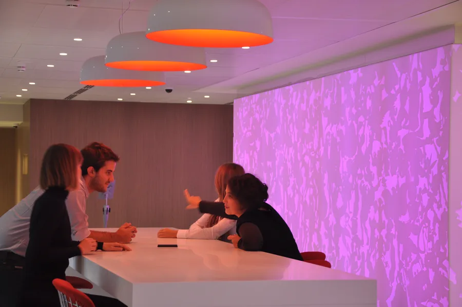 Occupied bar with Corian panels in purple-pink mode, employees socialising around the counter and cafe seating