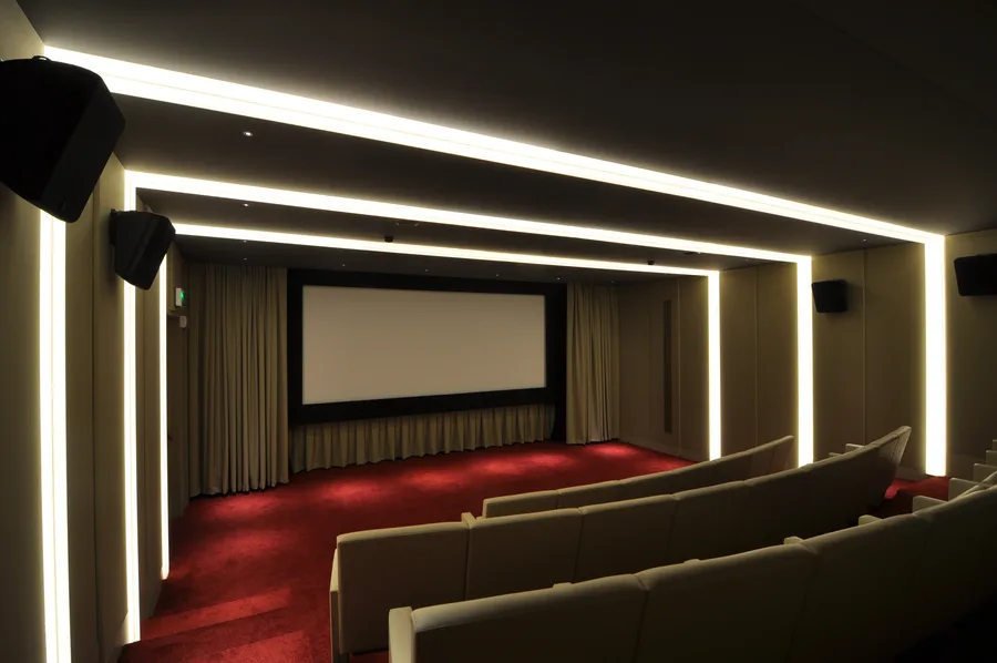 Full screening room view with multi-mode LED ambient lighting in neutral mode, vintage film reel decorative elements on walls