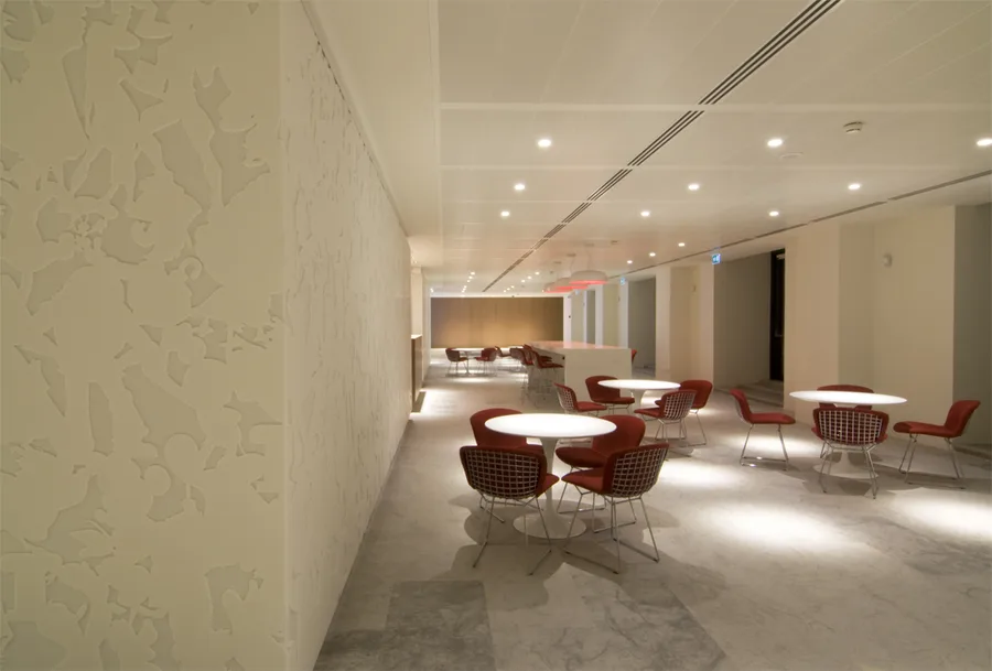 Cafe seating area with Corian relief wall panels, Bertoia Diamond chairs, Saarinen coffee tables, and controlled evening light through windows