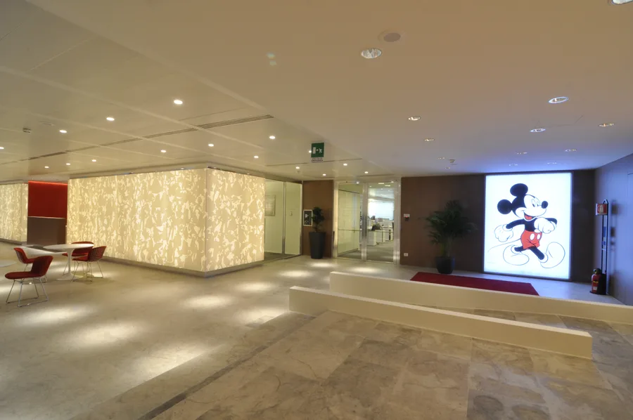 Full ground floor lobby with the Corian panel architectural volume, art gallery corridor, and backlit Mickey Mouse lightbox focal point
