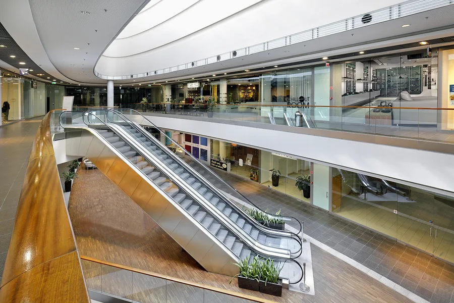 Interior: professional photograph of Drukarnia Mall retail corridor showing renovated common area finishes and tenant unit frontages