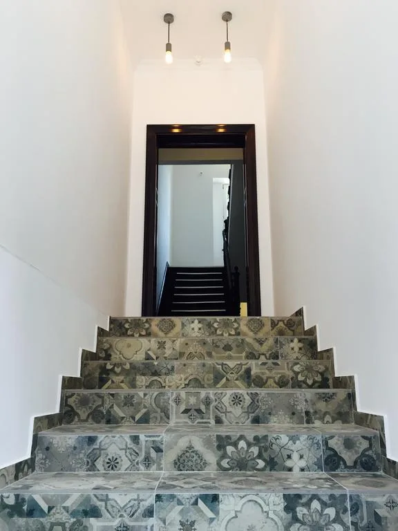 Staircase with patchwork cement tile risers, pendant lights, dark wood frame doorway, white walls