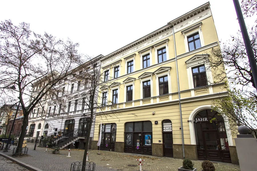 Yellow-painted building with adjacent lighter building, full neoclassical facade, ground floor commercial units, autumn bare trees