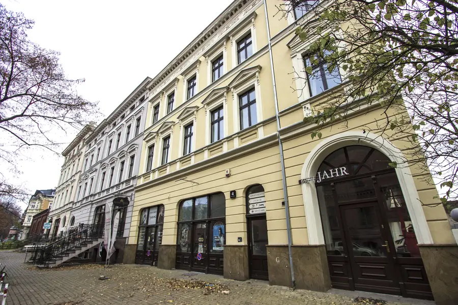 Yellow JAHR building close-up with arched entrance, JAHR signage, ornamental window surrounds, two buildings meeting at different colors