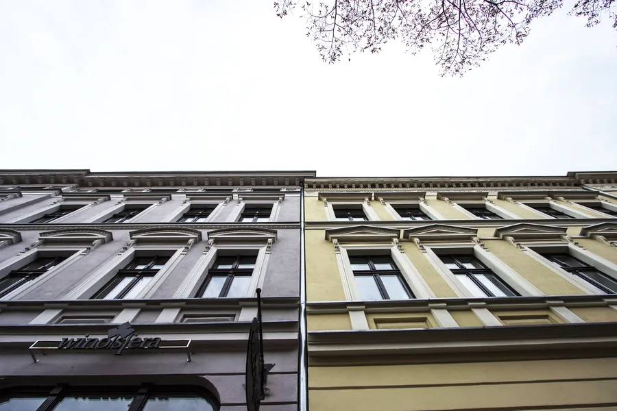 Two building facades looking straight up, different colors grey and yellow, ornamental details, overcast sky