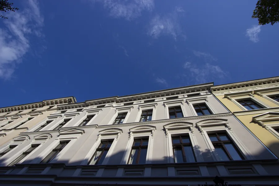 Building facade looking up against blue sky, white and grey neoclassical with window pediments, cornice details, dramatic perspective
