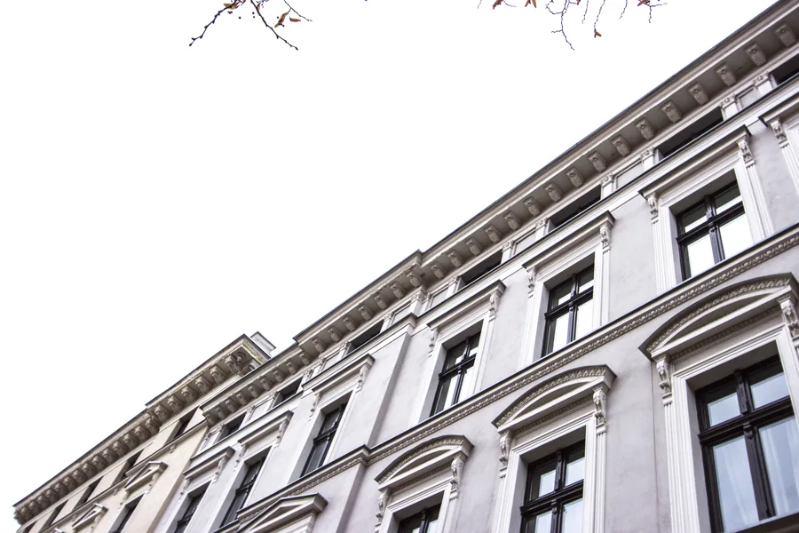 White and grey building facade looking up, autumn bare branches, fine cornice detailing, window pediments