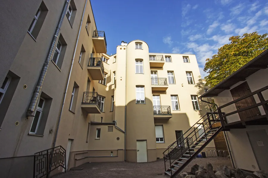 Inner courtyard with cylindrical staircase tower, balconies, warm yellow render, metal external staircase, blue sky