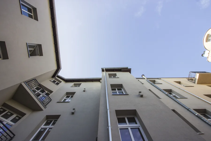 Courtyard looking straight up at multiple building wings meeting, drainpipes, balconies, blue sky, geometric composition
