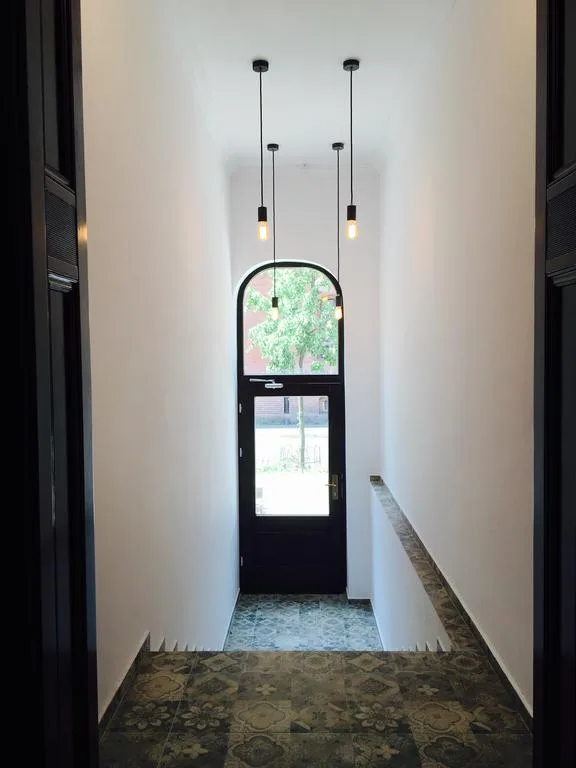 Building entrance hallway with patchwork cement tile floor, arched glass door, pendant lights, narrow perspective