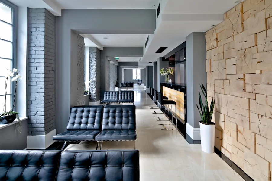 Lobby corridor with Barcelona chairs, 3D wood block wall treatment, and backlit onyx bar counter glowing amber against natural stone walls