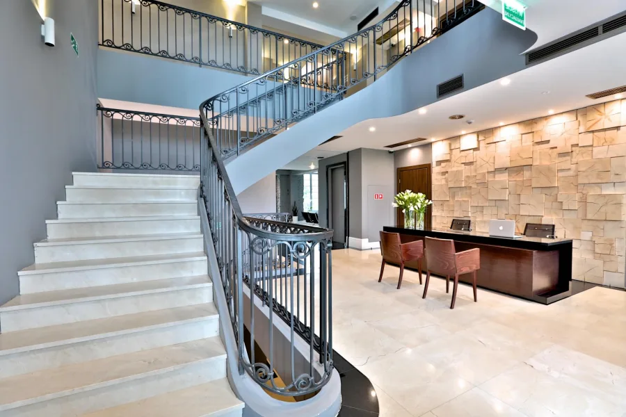 Reception area with sculptural open-tread oak staircase, glass balustrade, and natural stone feature wall in the New Manor