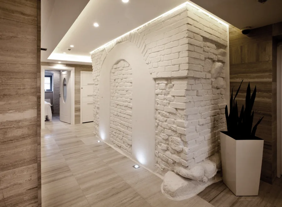 Spa corridor beneath white-painted heritage barrel-vault brick ceiling with travertine floor and woven vinyl accents