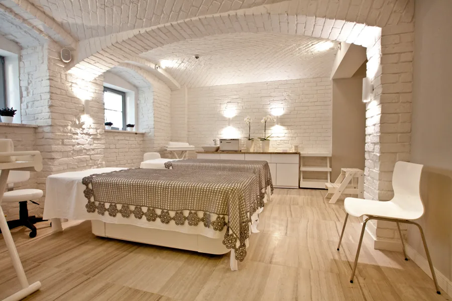 Spa treatment room under white-painted barrel-vault brick ceiling with lace-edged treatment covers and orchid styling