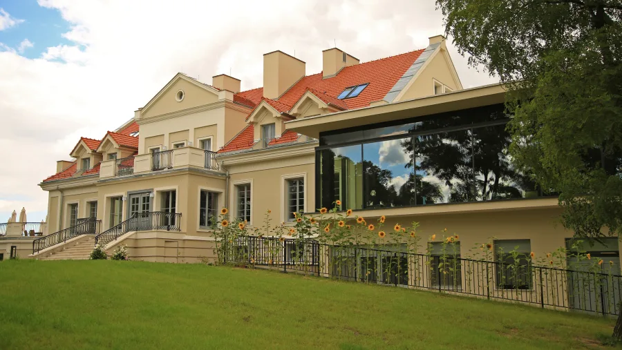 Summer exterior facade with blooming sunflowers in the foreground and the heritage manor building bathed in warm daylight