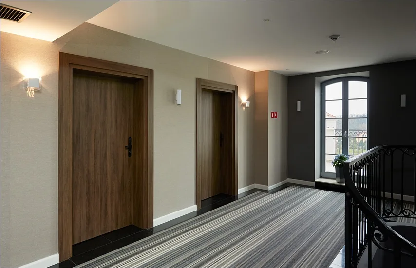 Hotel corridor with room doors, striped carpet runner, and wrought iron banister detail