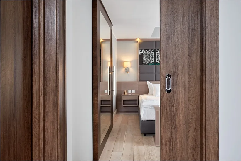 Room entrance with walnut sliding doors and peek through to guest room with perforated headboard