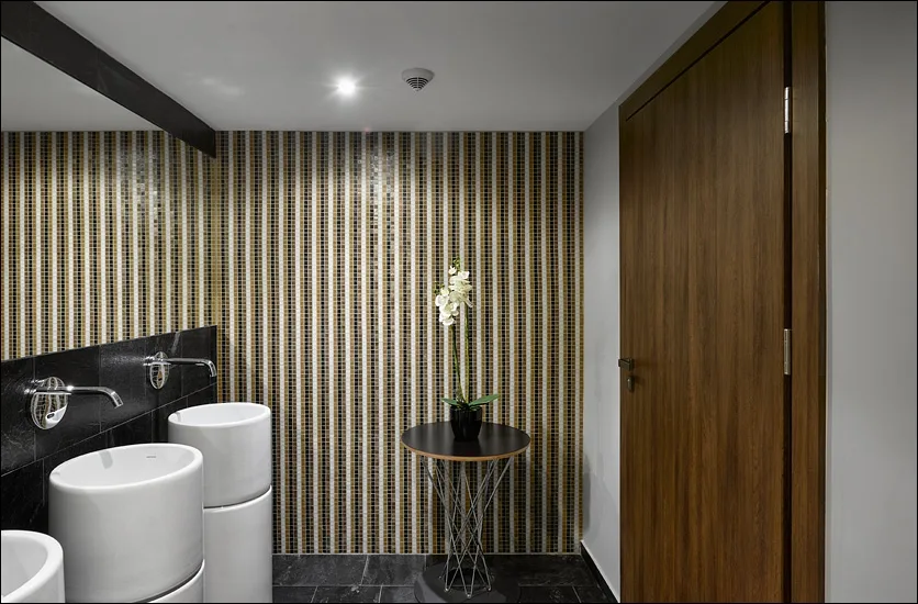 Spa restroom with mosaic striped wall, freestanding basins, orchid, and walnut door detail