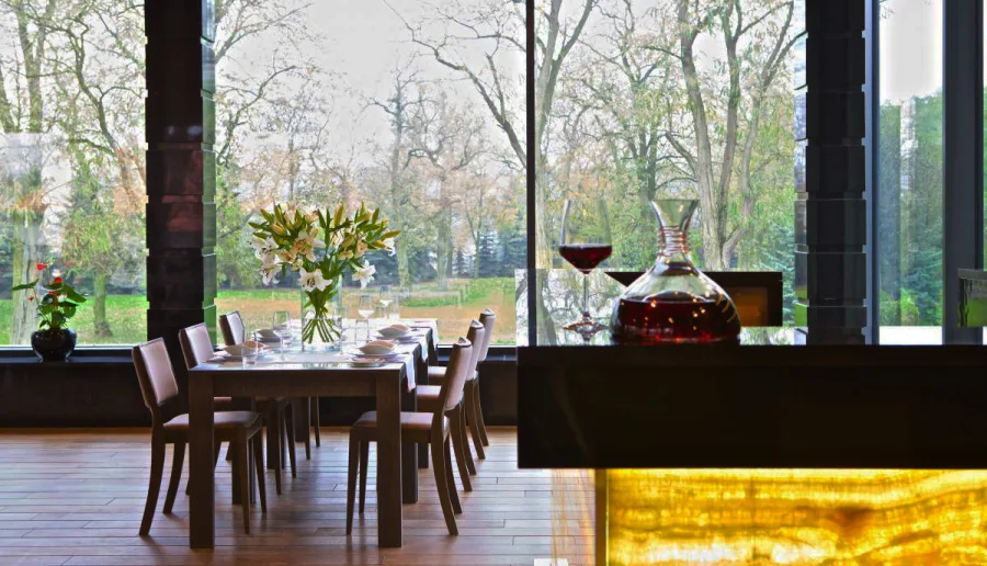 Restaurant detail showing set table with wine decanter and panoramic autumn park views through glazing