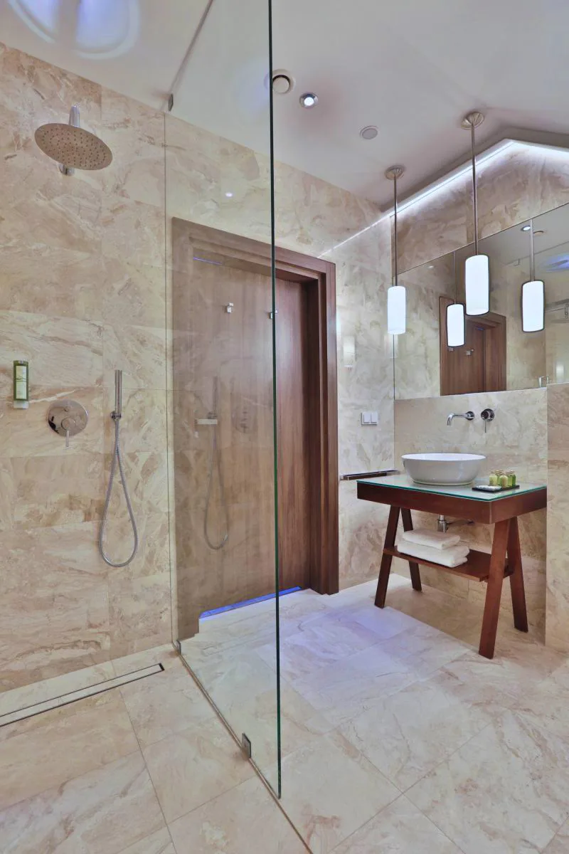 Bathroom with natural stone walls, rain shower, walnut vanity, and pendant lights