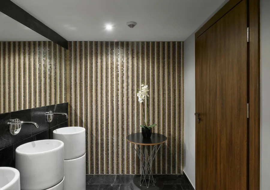 Spa bathroom with vertical striped mosaic wall, white freestanding basins, orchid, and walnut door
