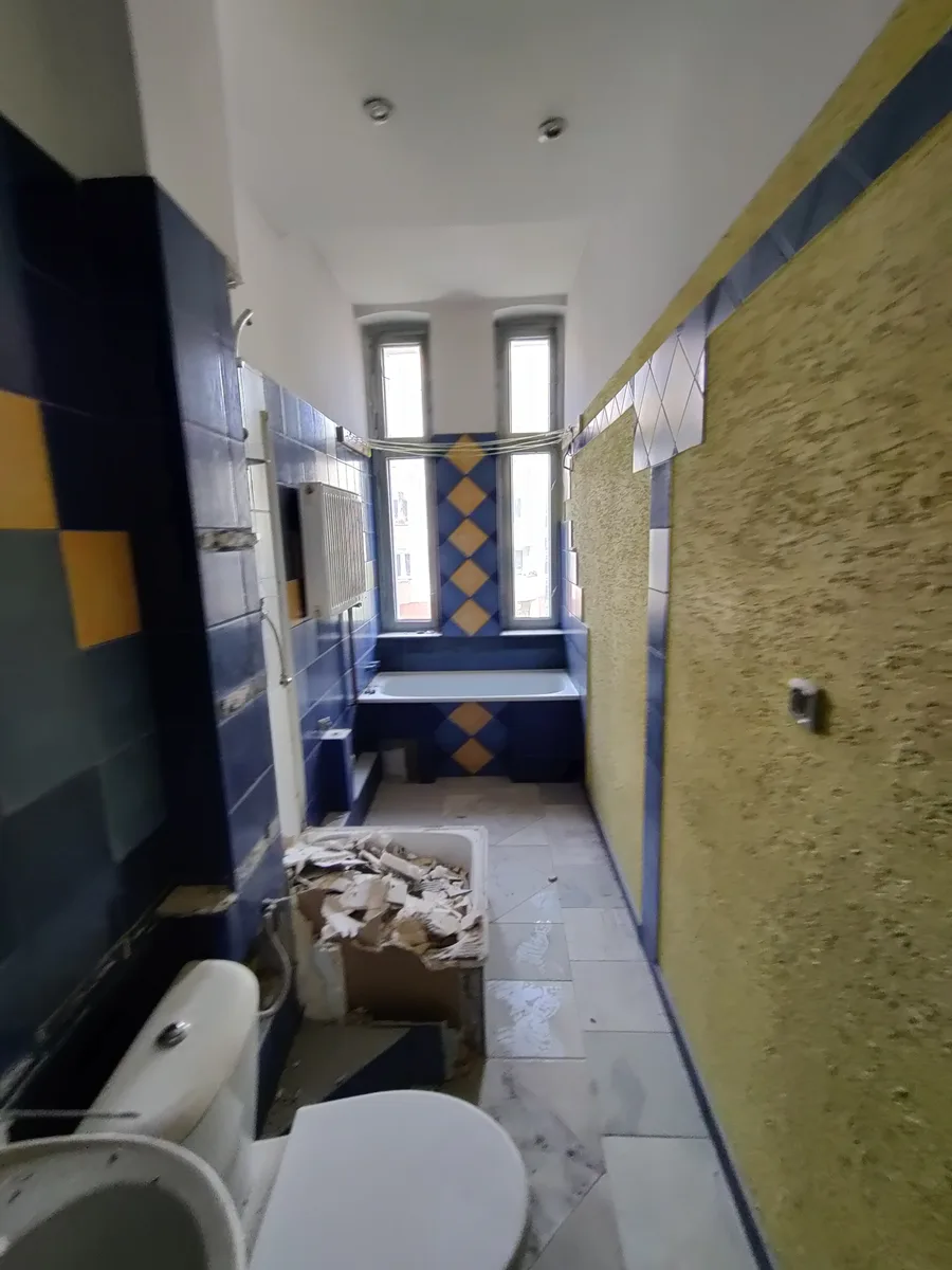 Before: pre-renovation bathroom in tenement showing blue and yellow wall tiles, bathtub, exposed plaster, and construction debris at Hetmanska 20 kamienica