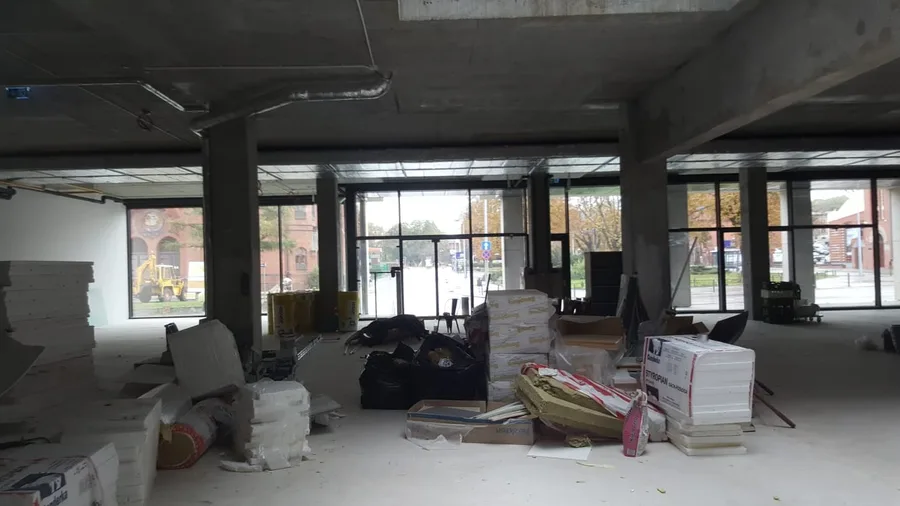 Documentary: main hall scale photograph facing the full-width floor-to-ceiling glazed facade with deep concrete beams, column grid, Isover insulation materials, and historic red-brick Prussian building visible outside