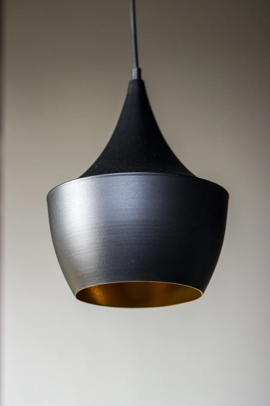 Detail: single Tom Dixon Beat pendant with matte black exterior and hammered gold interior in product-quality portrait