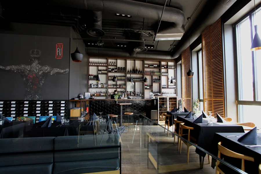 Interior: upper floor lounge area with warrior mural, wine display wall, leather banquettes, and glass partition