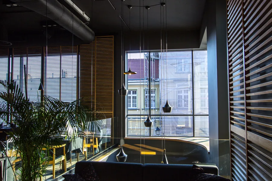 Interior: upper floor dining with Tom Dixon pendants, venetian blinds, dark tablecloths, Wishbone-style chairs, and double-height glazing