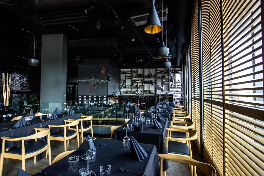 Interior: upper floor dining from different angle with warrior mural visible, wine wall, and venetian blinds along windows