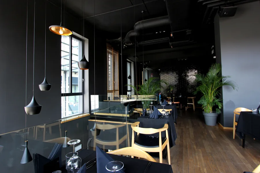 Interior: upper floor dining long table with venetian blinds and Tom Dixon pendants, black tablecloths, and oak chairs
