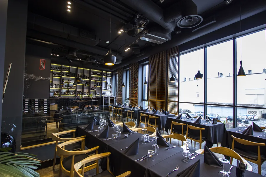 Interior: upper floor dining toward wine wall with warrior mural, backlit shelves, and evening atmosphere