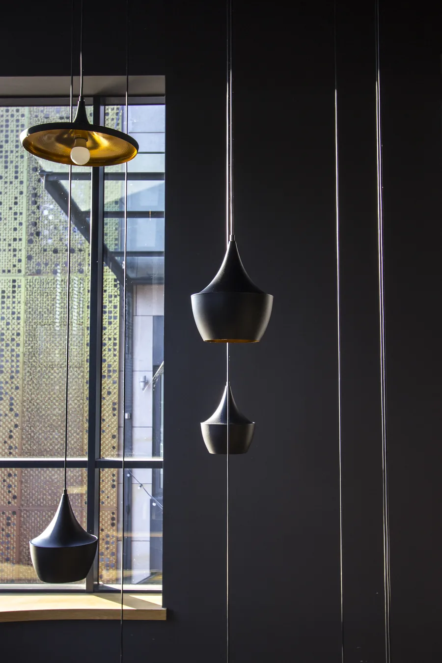 Detail: Tom Dixon Beat pendant trio with three Tall variants silhouetted against window and gold Beat Wide